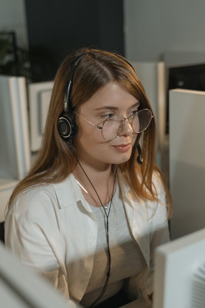 Services A young woman with eyeglasses and headphones working in a call center.