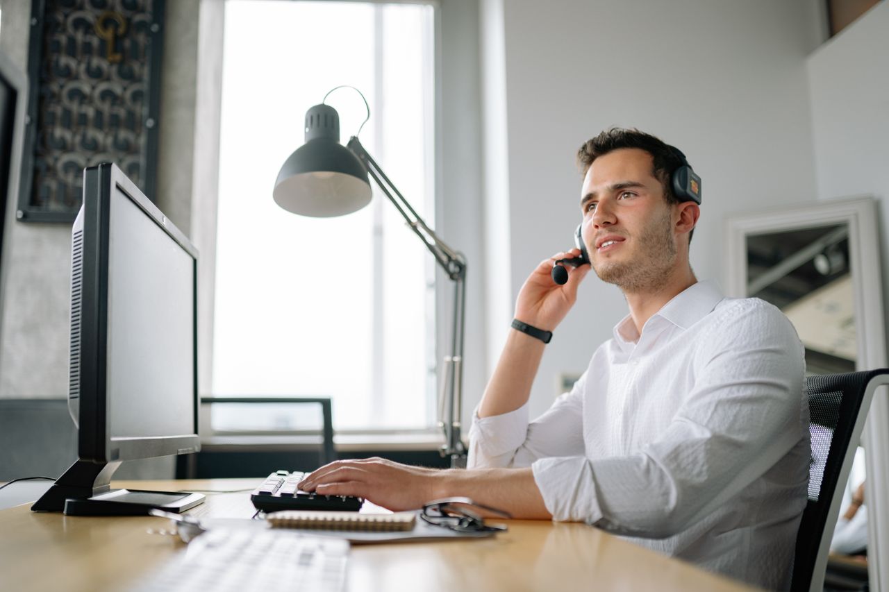 Services Male call center agent with headset working at desk, providing excellent customer service.